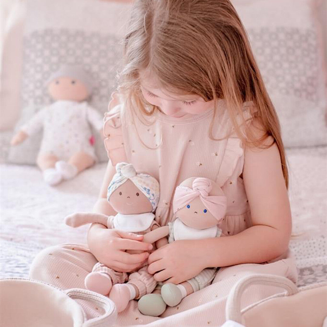 Een kind zit op bed en knuffelt twee Bonikka lappenpoppen met verschillende hoofdbanden.