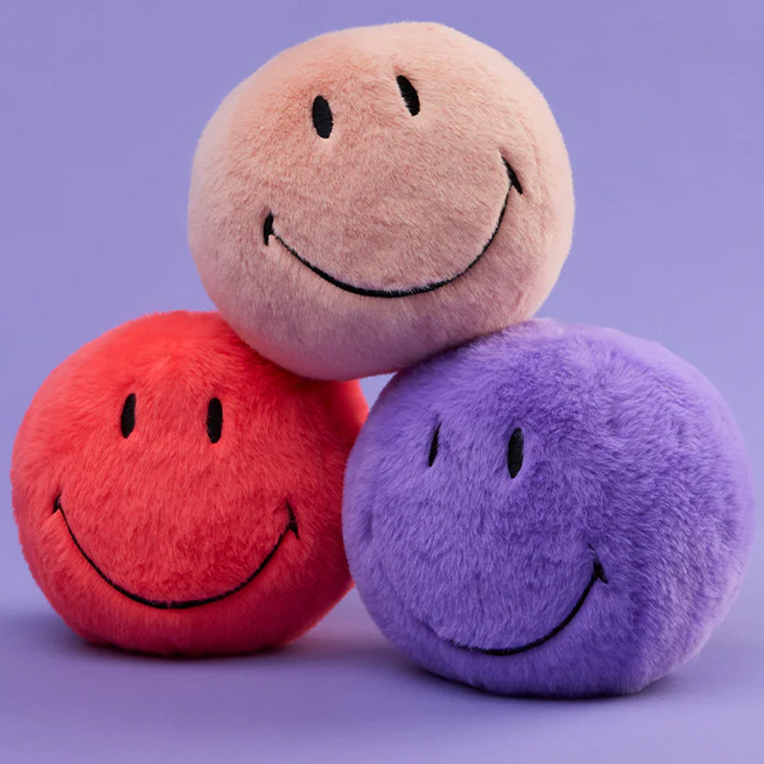 Drie bon ton toys pluchen knuffelballen in roze, rood en paars, gestapeld op een paarse achtergrond.