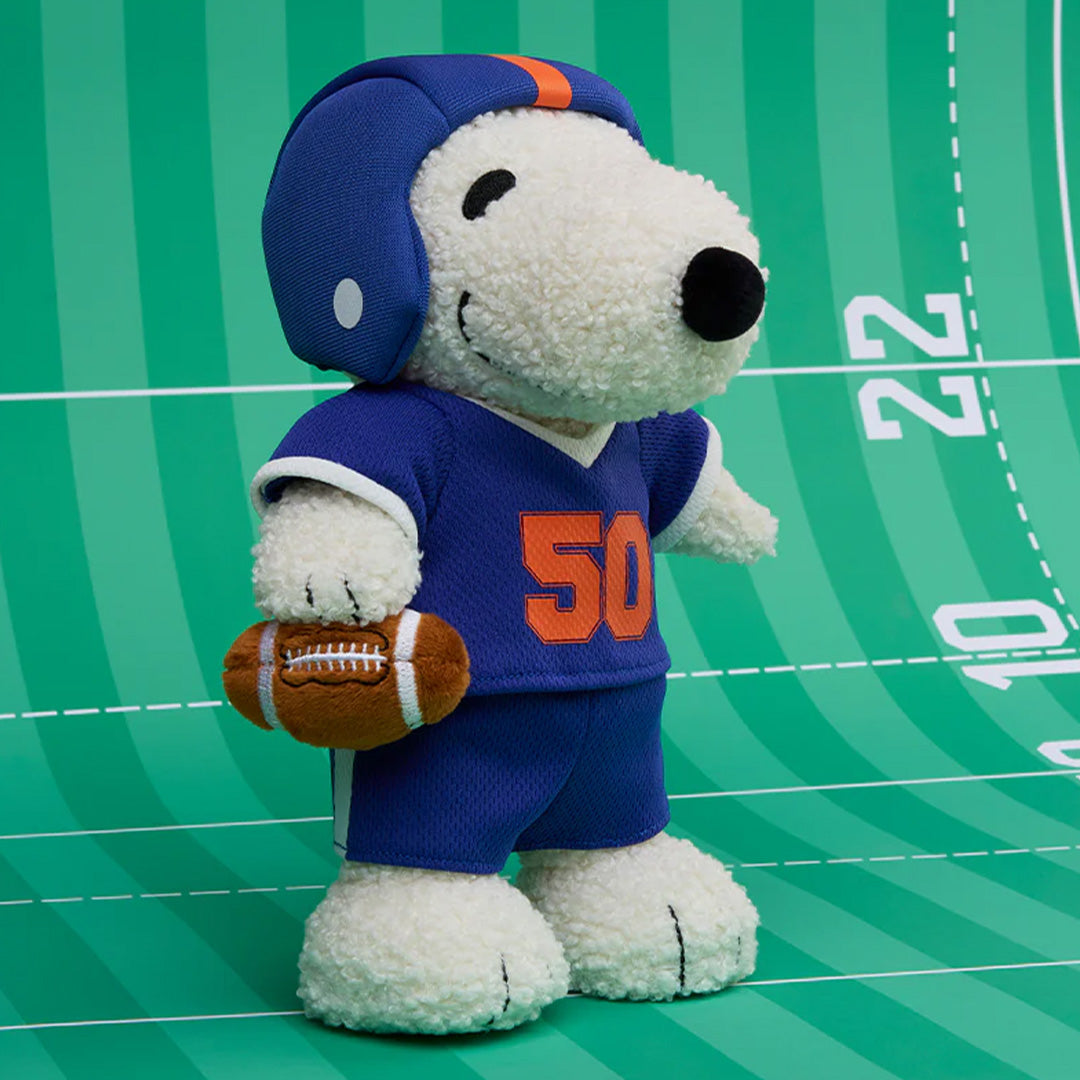 Pluchen knuffelhond Snoopy in American football outfit op een groen speelveld.