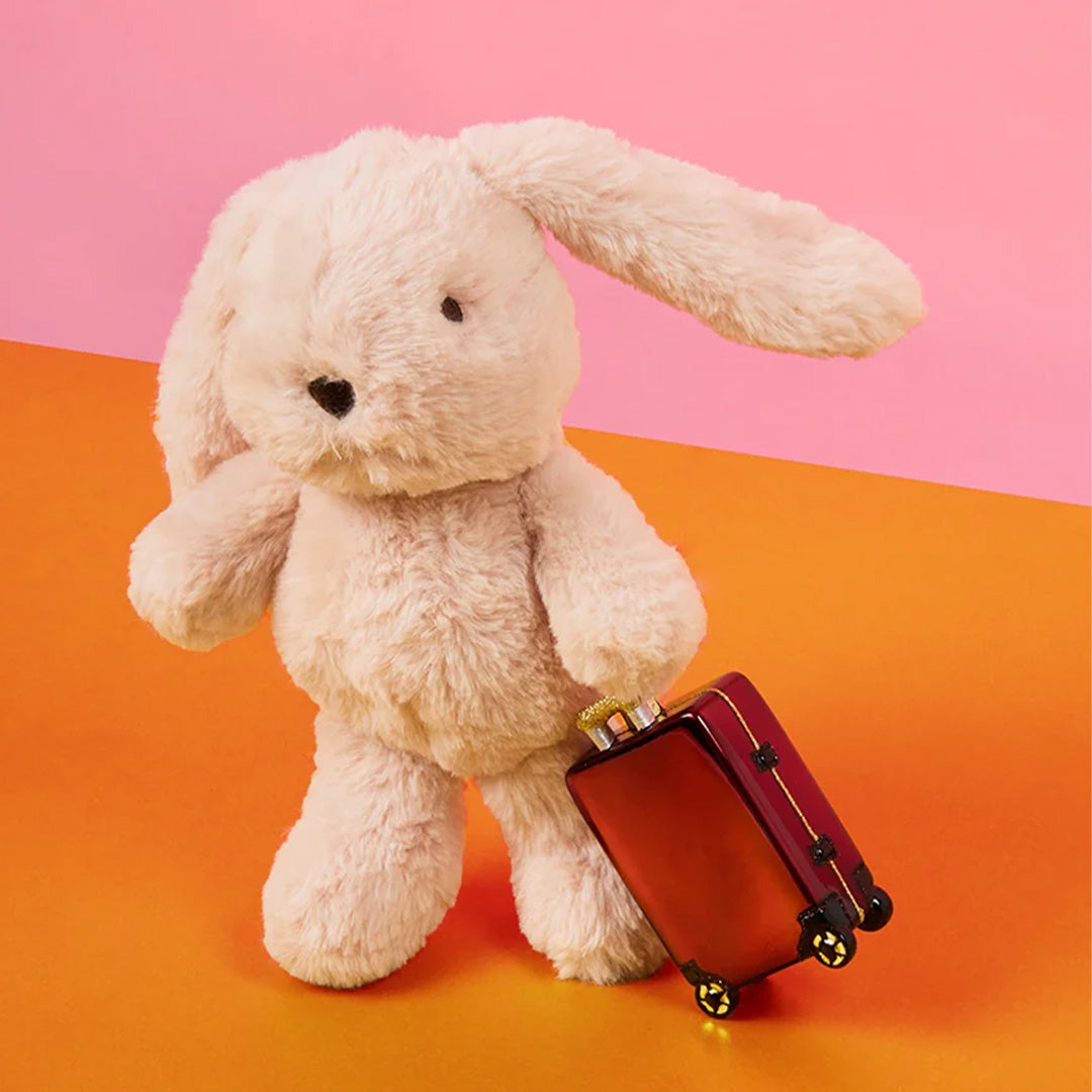 Bon ton toys pluchen knuffelkonijn Bubbles Bunny trekt een rood koffertje op een oranje en roze achtergrond.