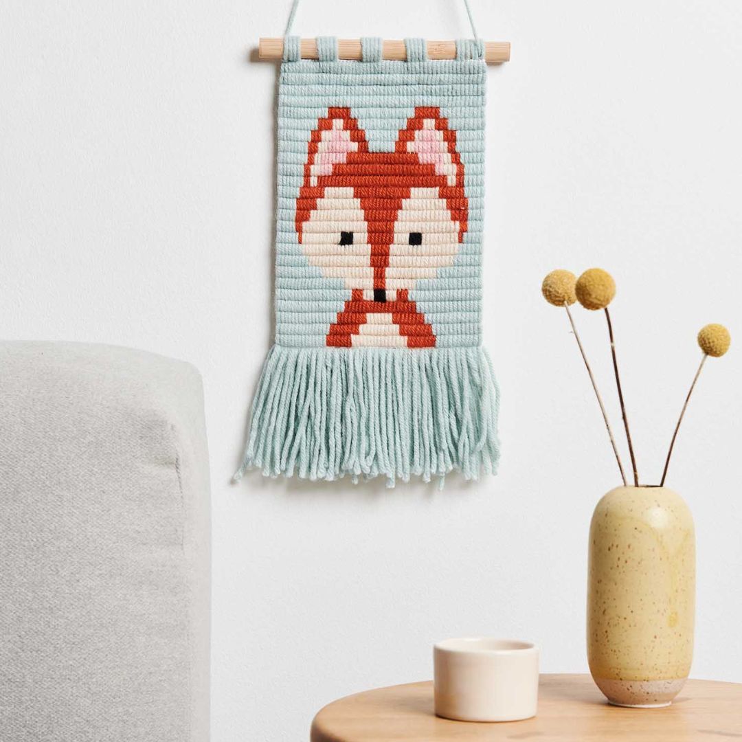 Geborduurde muurhanger met vos hangend aan een witte muur boven een bijzettafel.