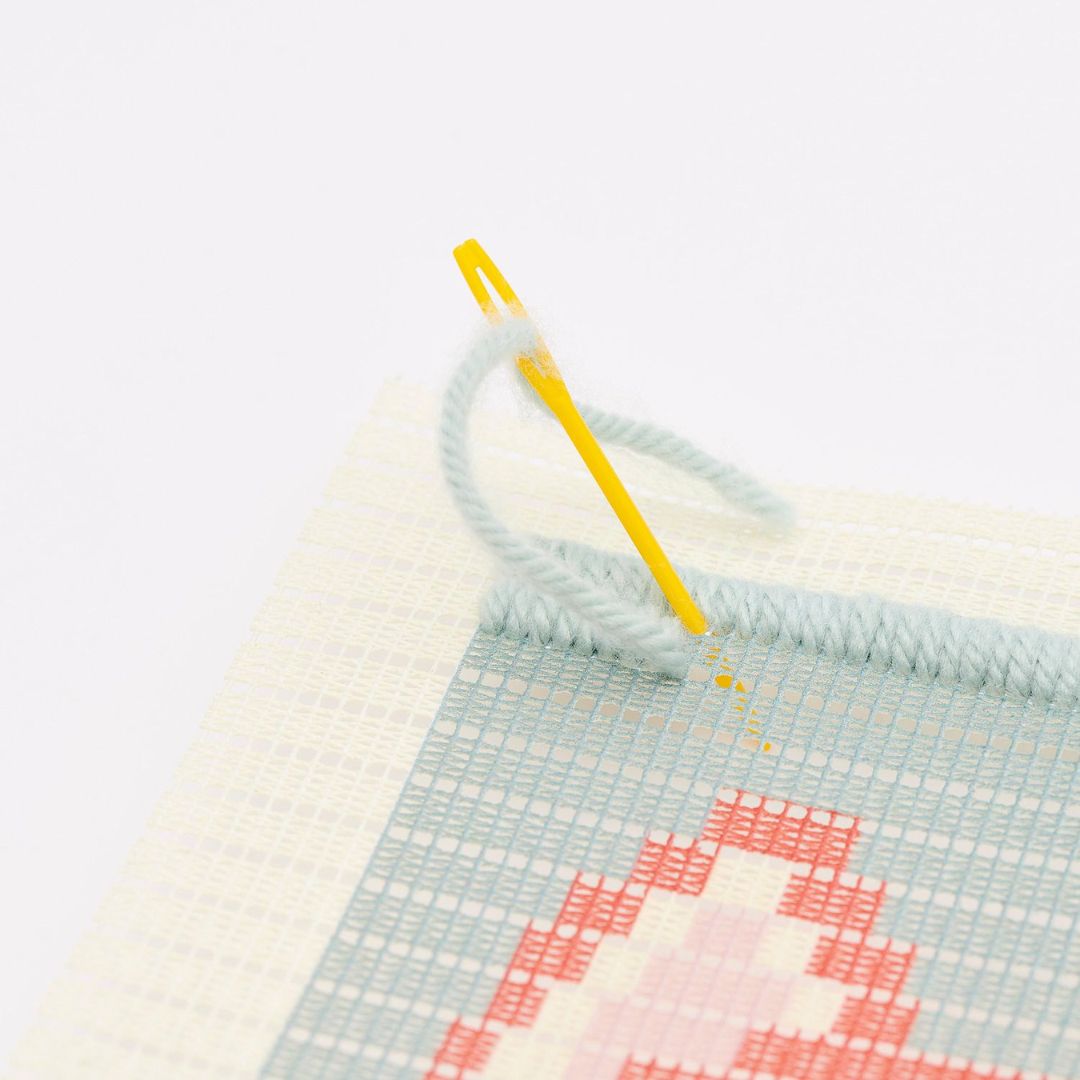 Detail van een geel borduurnaald met lichtblauwe draad in een canvas voor een vosontwerp.
