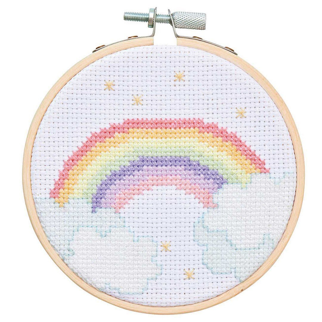 Een Rico Design kruissteek borduurwerk van een regenboog met wolken en sterren in een houten ring.