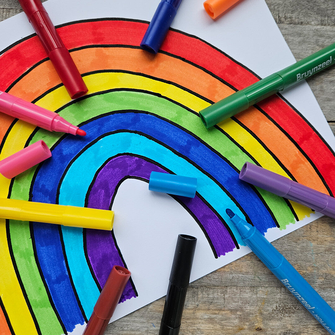 Een tekening van een regenboog gemaakt met Bruynzeel viltstiften, met enkele stiften en doppen eromheen op een houten ondergrond.
