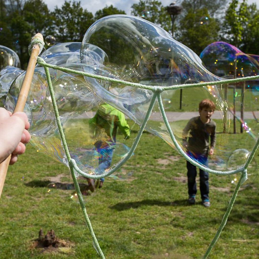 Een kind kijkt naar een grote zeepbel die wordt gemaakt met een Bubble Lab bellenblaasstok in een park.