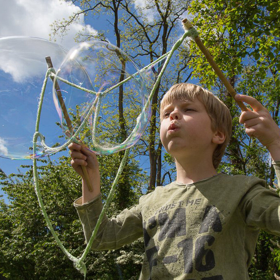 Een kind blaast een grote zeepbel met een Bubble Lab bellenblaasstok buiten in de zon.