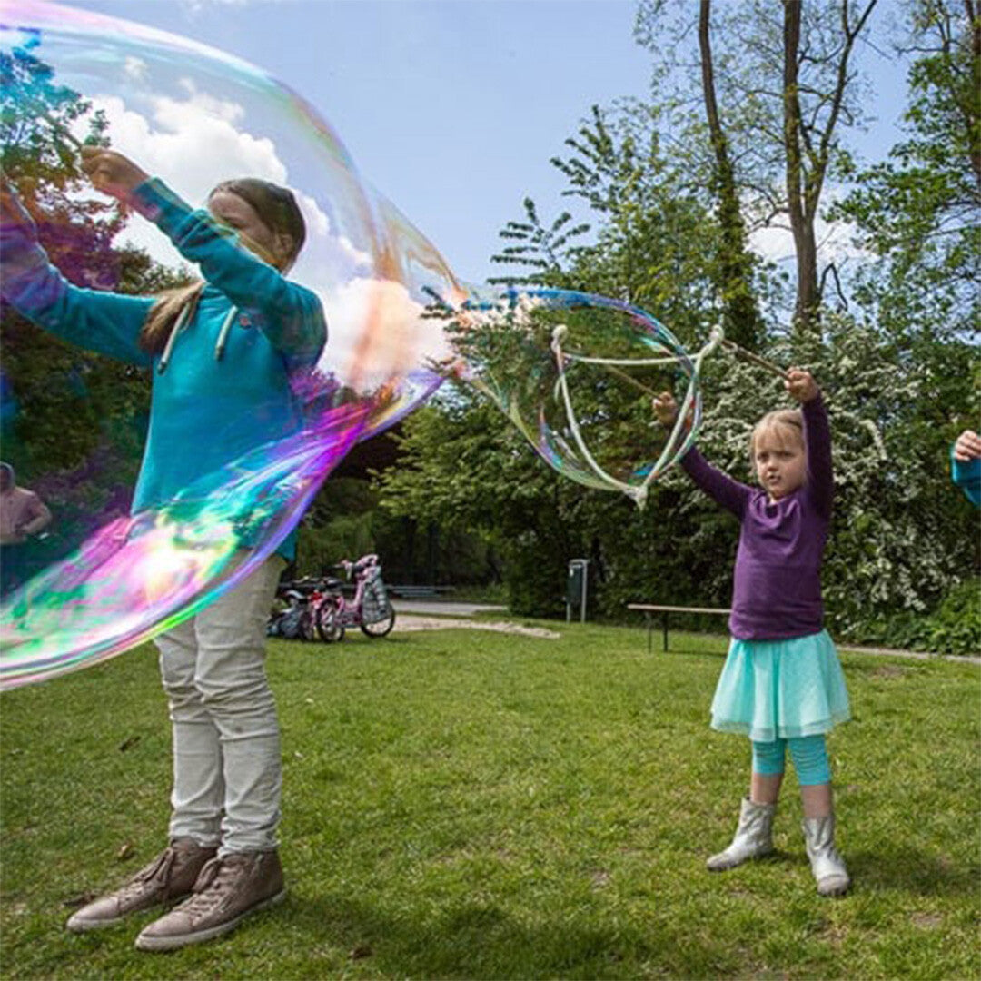 Twee kinderen maken grote bellen met het Bubblelab bellenblaasspeelgoed in een park.