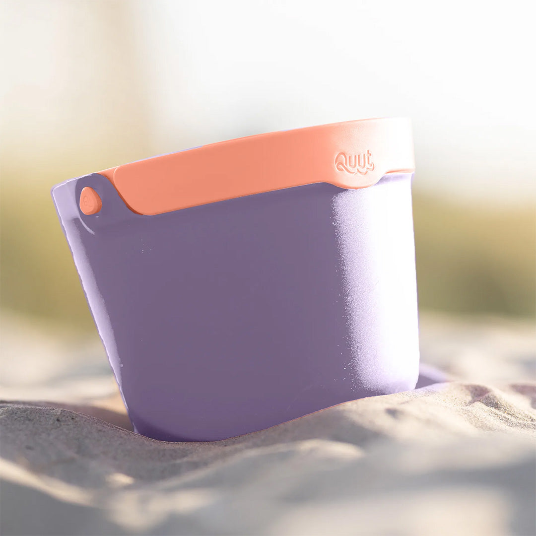 Quut paarse strandemmer met oranje handvat staat in het zand op het strand.