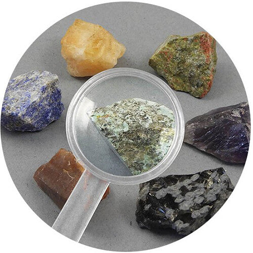Detail van diverse ruwe stenen en mineralen, met een vergrootglas gericht op een groene steen.