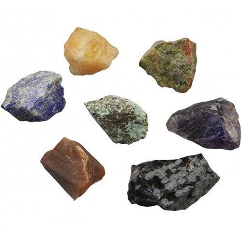 Een collectie van zeven ruwe, kleurrijke stenen en mineralen op een witte achtergrond.