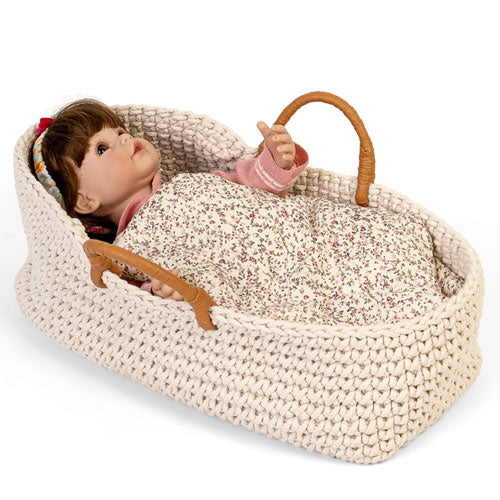By Astrup gebreide poppenreiswieg met een pop erin, bedekt met een gebloemde deken.