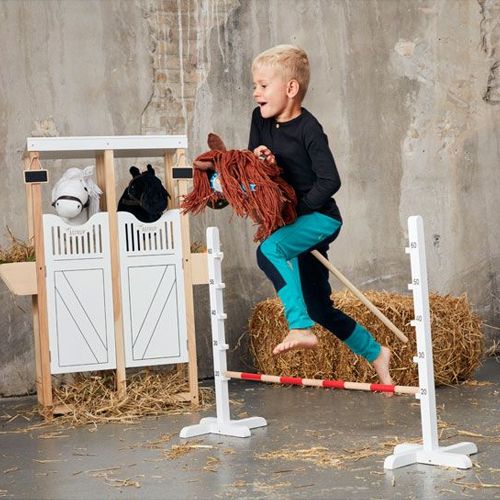 Een kind springt met een stokpaard over de by astrup houten hindernis.