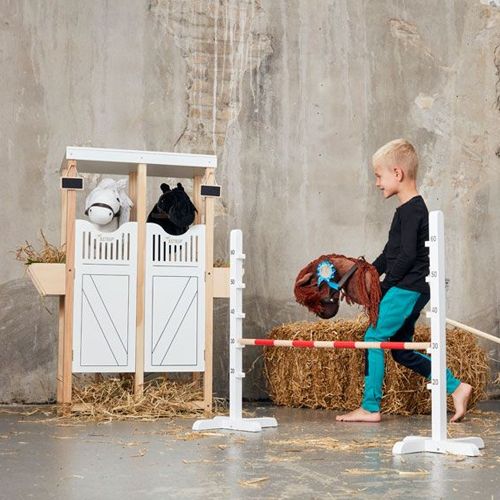 Een kind loopt met een stokpaard naast de by astrup houten hindernis.