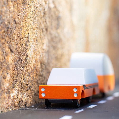 Candylab houten speelgoedvrachtauto 'Orange Mule' met witte kap trekt een caravan op een weg.