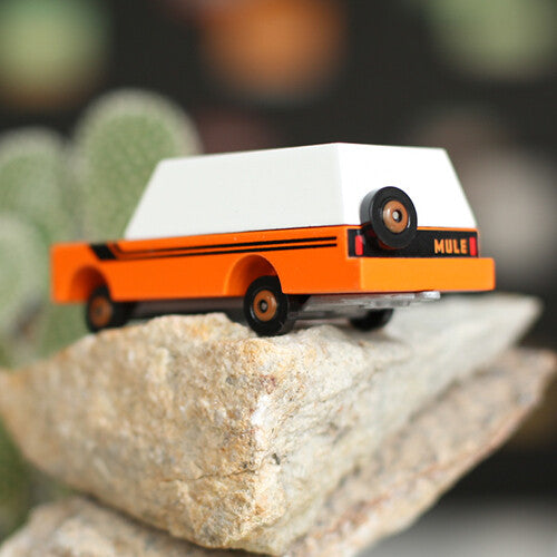 Candylab houten speelgoedvrachtauto 'Orange Mule' met witte kap en reservewiel op een rots.