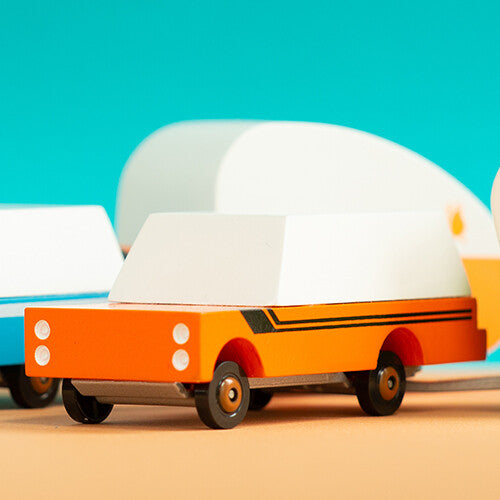 Candylab houten speelgoedvrachtauto 'Orange Mule' met witte kap, met andere speelgoedvoertuigen op de achtergrond.
