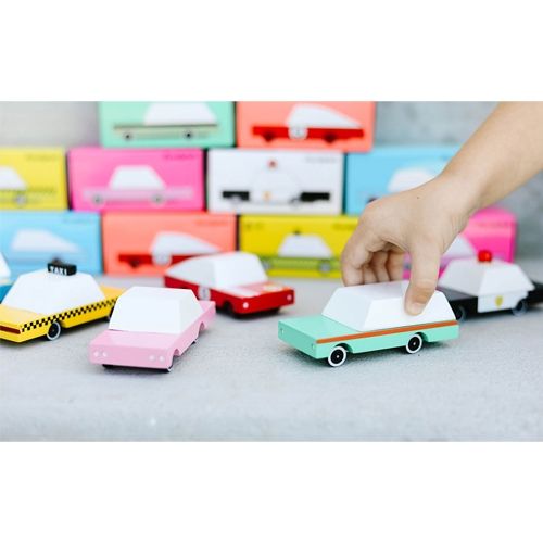 Een hand pakt een Candylab houten speelgoedauto uit een collectie van diverse gekleurde speelgoedauto's met verpakkingen op de achtergrond.