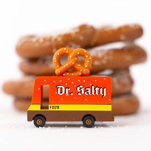 Candylab Dr. Salty speelgoedvrachtauto met pretzel op het dak, staand op een witte ondergrond met zoutkorrels en echte pretzels op de achtergrond.