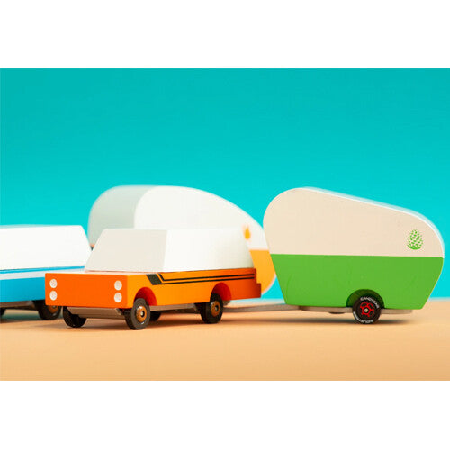 Candylab houten speelgoedcaravan in groen en wit, gekoppeld aan een oranje speelgoedauto, met blauwe achtergrond.