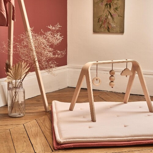 Charlie Crane houten babygym op een roze speelmat in een kamer met een rode muur.
