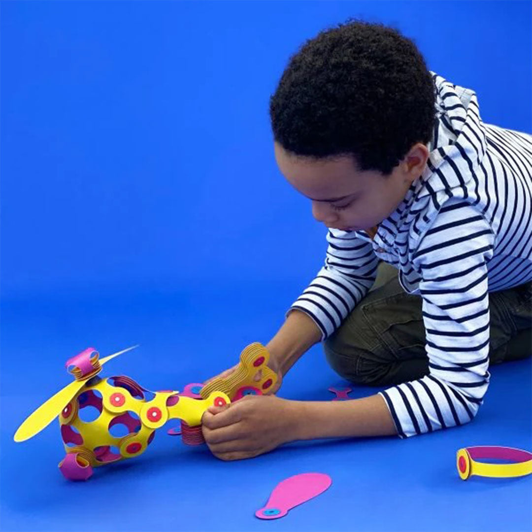 Een jongen knielt op een blauwe ondergrond en bouwt een helikopter met de Clixo magnetische bouwset.