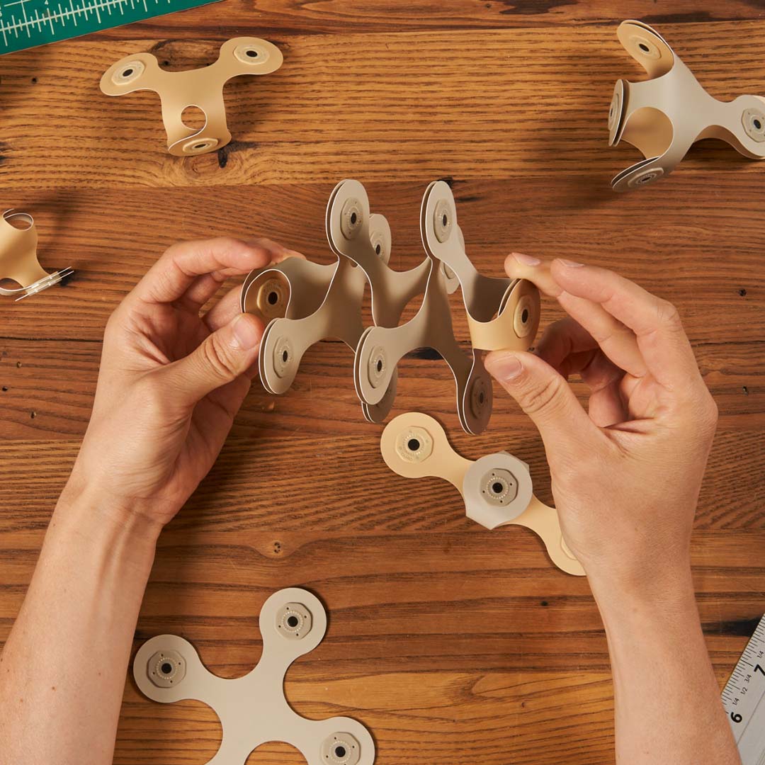 Twee handen die Clixo magnetische bouwstukken in elkaar zetten op een houten tafel.
