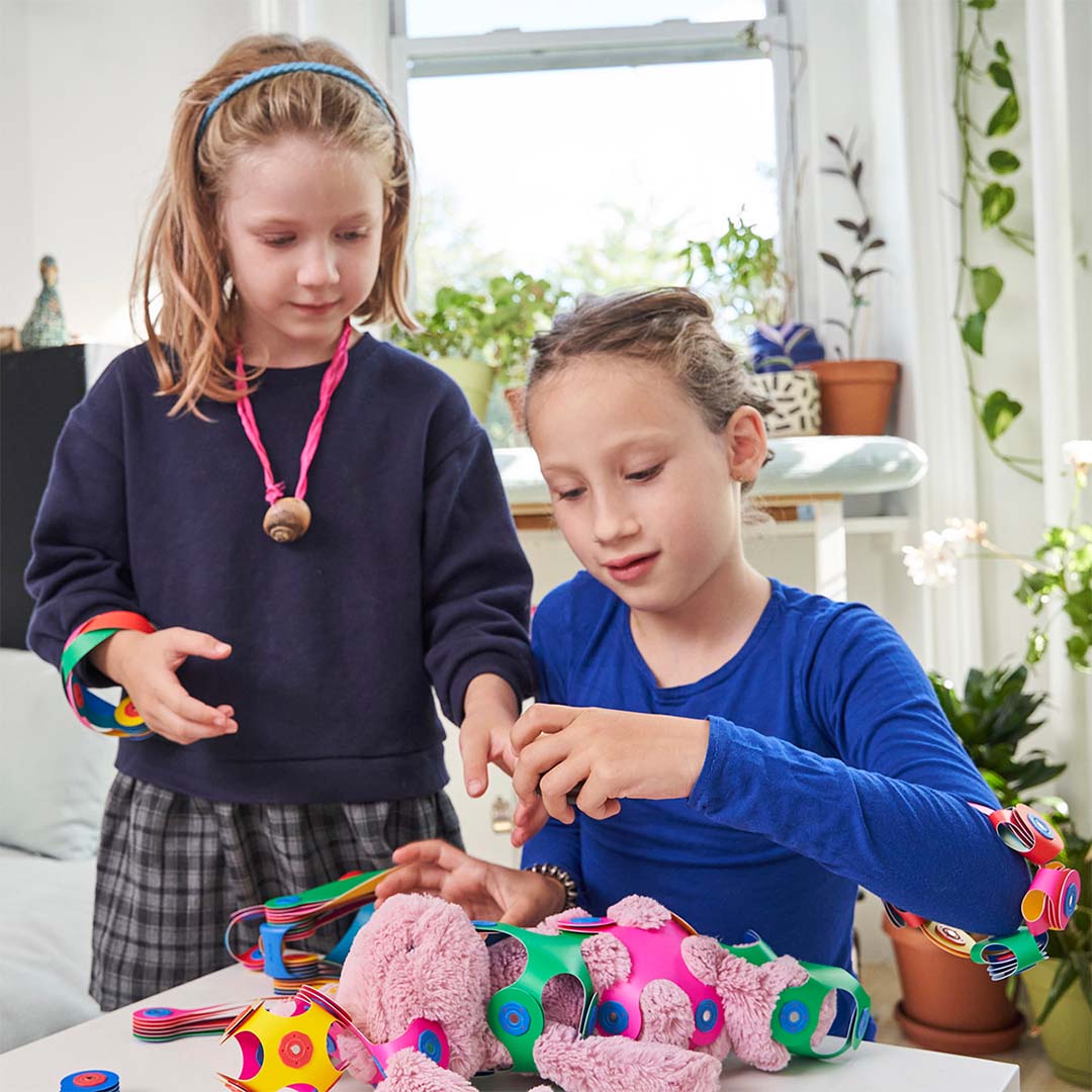 Twee meisjes spelen binnen met de Clixo magnetische bouwset en bouwen een kleurrijk dier.