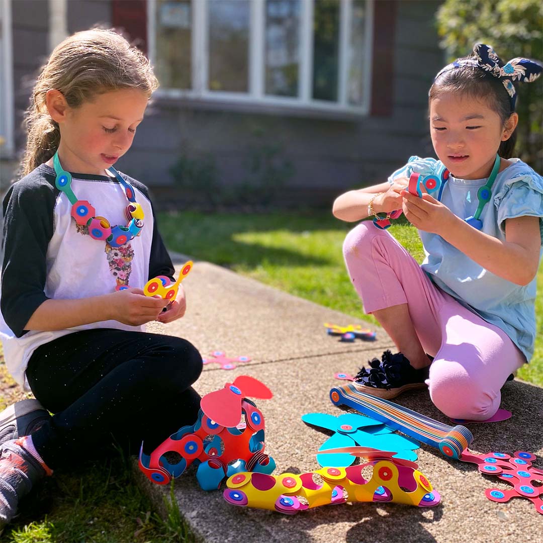 Twee meisjes spelen buiten met de Clixo magnetische bouwset en bouwen kleurrijke figuren en dieren.
