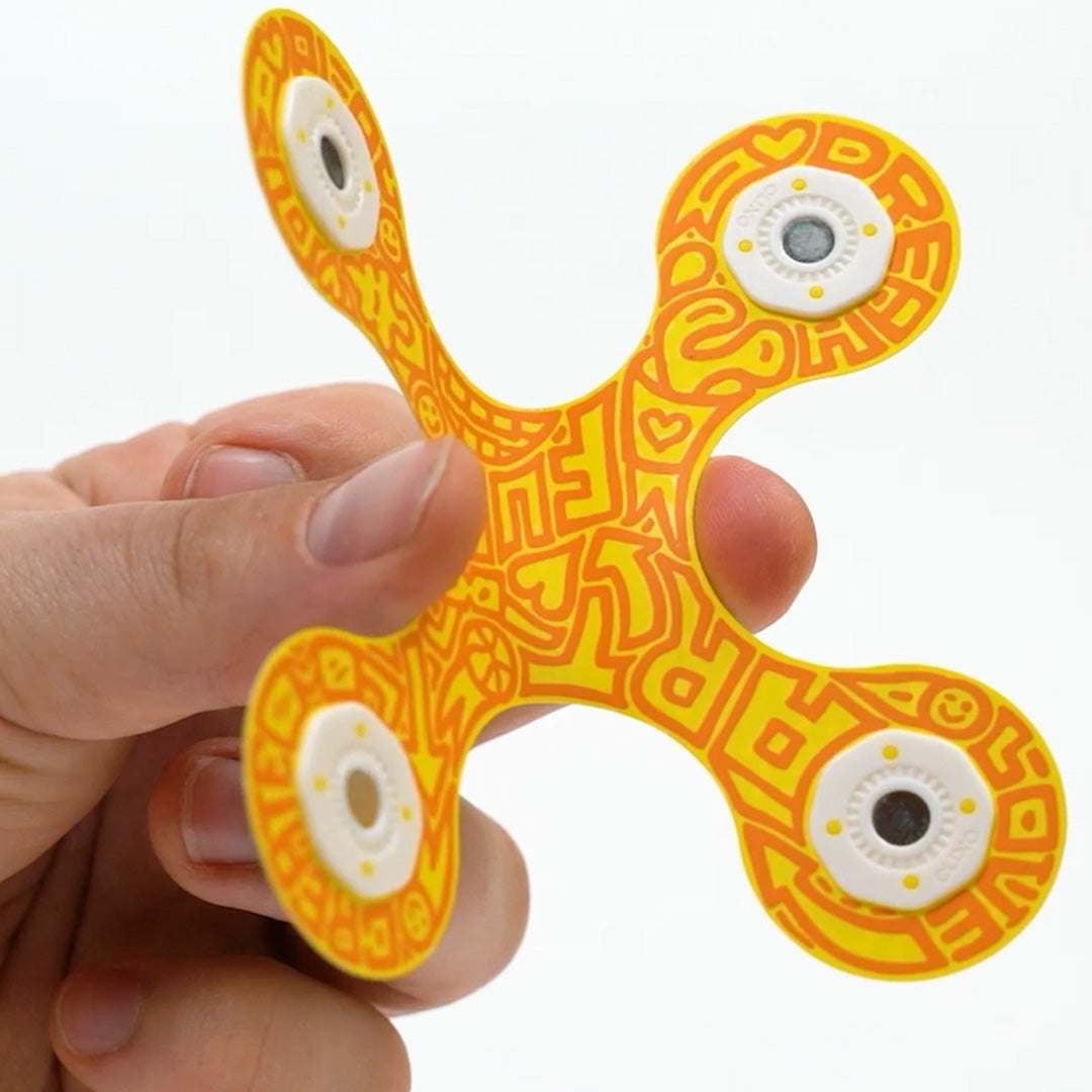 Een hand houdt een geel Clixo magnetisch bouwstuk met abstract patroon vast.