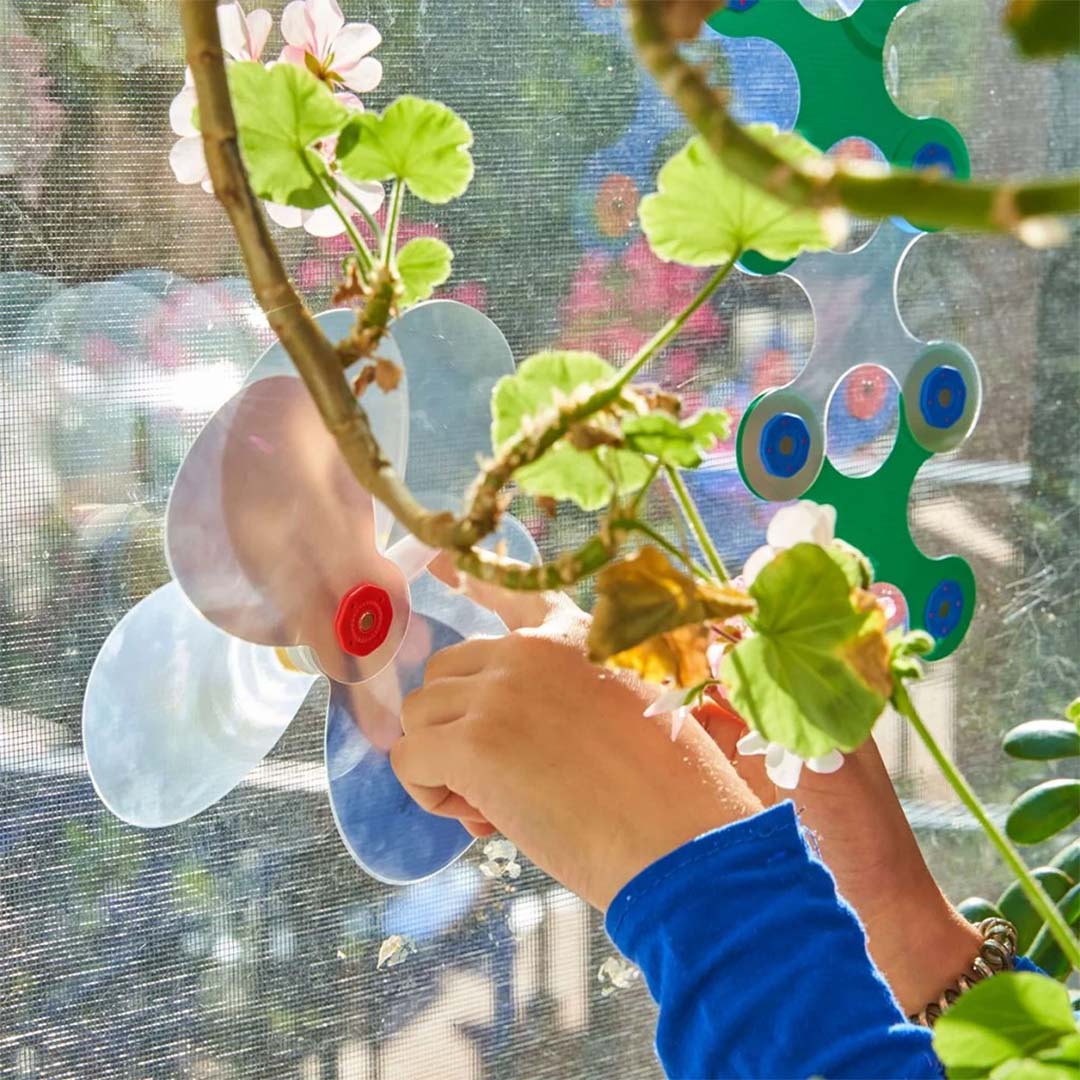 Kinderhanden bevestigen een Clixo magnetisch bouwonderdeel in de vorm van een propeller op een raam.