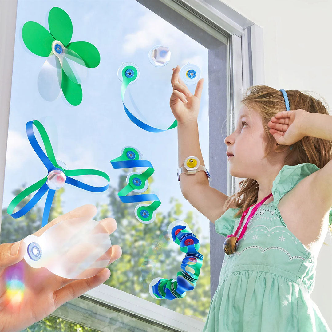 Een meisje kijkt naar verschillende Clixo magnetische creaties die op een raam zijn bevestigd.