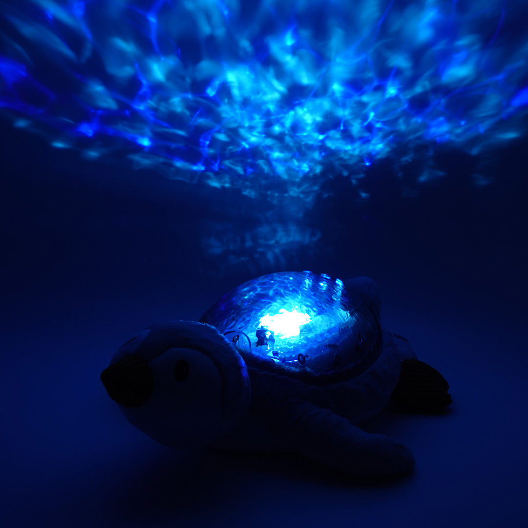cloud.b knuffelpinguin met nachtlamp die blauwe watergolven projecteert in een donkere kamer.