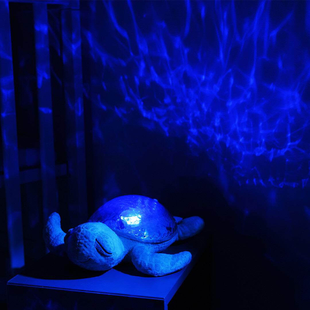De cloud.b knuffelschildpad projecteert blauwe watergolven op de muur in een donkere kinderkamer.