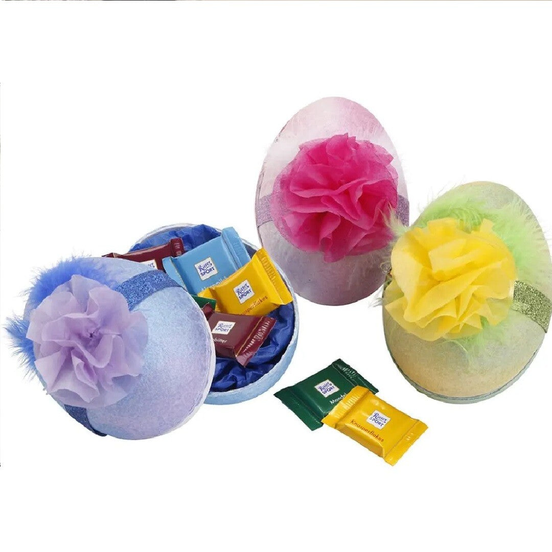 Drie versierde paaseieren met zijdepapier bloemen en linten, met chocolade ernaast.
