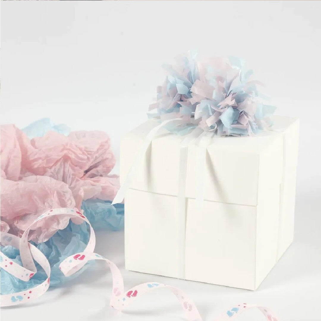 Een witte cadeaubox versierd met een roze en blauwe pom-pom van zijdepapier, met extra zijdepapier en lint.