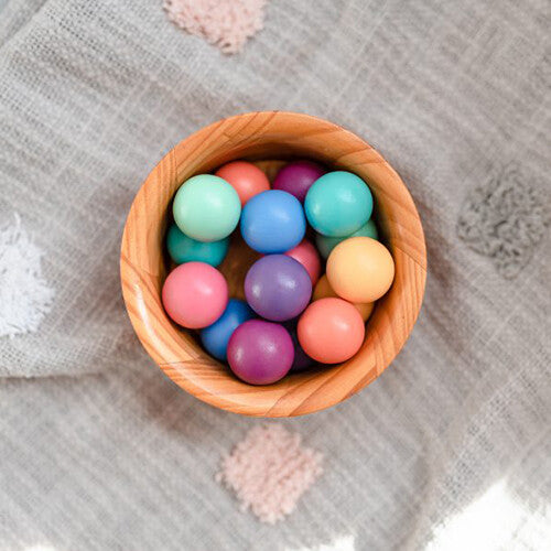 Een houten kom gevuld met diverse pastelkleurige knikkerbaanballen op een grijze deken.