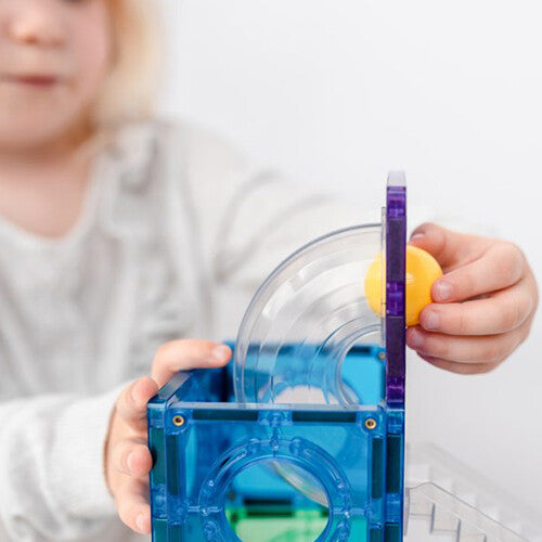 Een kind plaatst een gele knikkerbaanbal in een blauwe Connetix knikkerbaan.