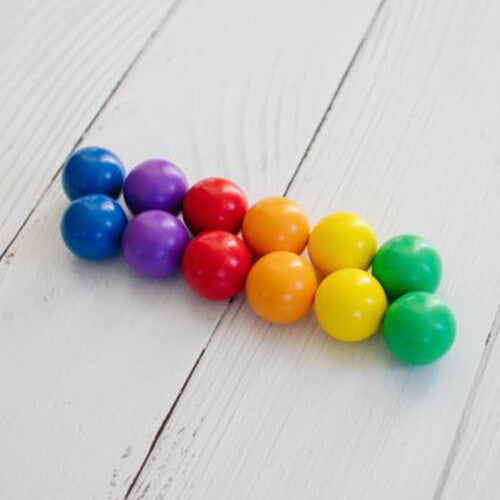Twaalf Connetix knikkerbaanballen in regenboogkleuren liggen op een witte houten ondergrond.