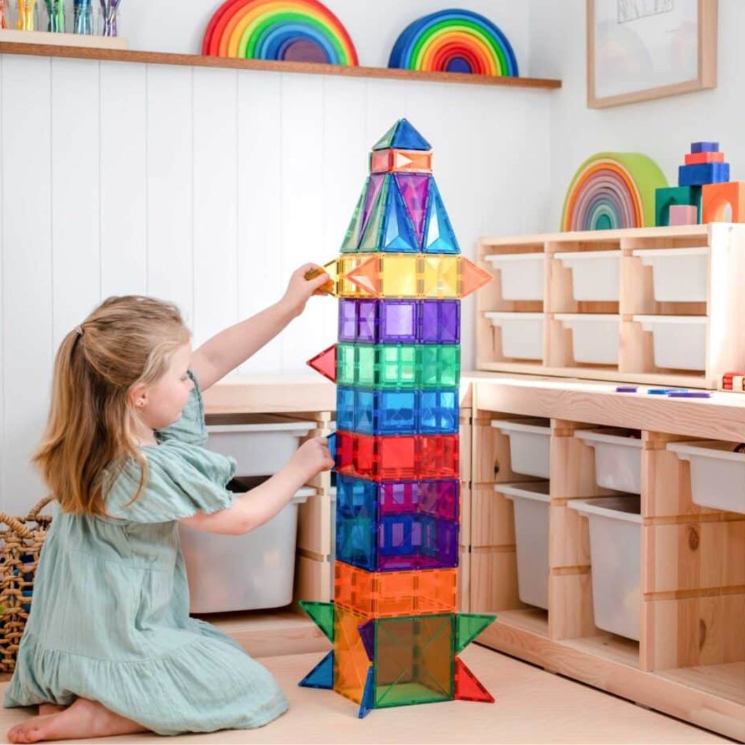 Een meisje bouwt een hoge, kleurrijke raket van Connetix magnetische tegels.