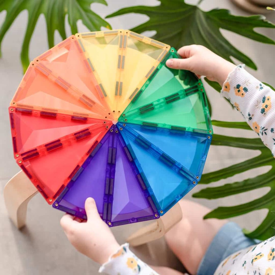 Kinderhanden houden een grote platte cirkel vast, gemaakt van Connetix magnetische tegels in regenboogkleuren.
