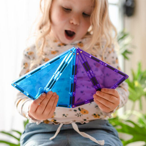 Een kind kijkt verrast terwijl het blauwe en paarse Connetix magnetische tegels vasthoudt die een 3D-vorm vormen.