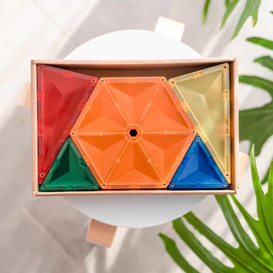 Connetix magnetische tegels in regenboogkleuren, waaronder zeshoeken en driehoeken, liggen in een doos.