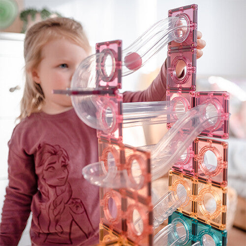 Een kind speelt met de Connetix magnetische tegels knikkerbaan in pastelkleuren, met een bal in de baan.