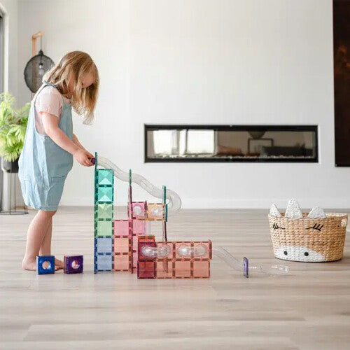 Een kind speelt met de Connetix pastel knikkerbaan van magnetische tegels in een woonkamer.
