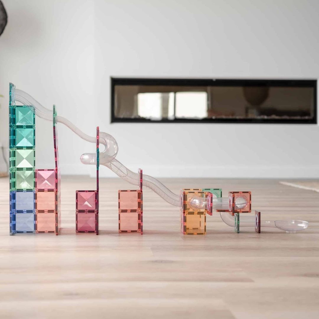 Een lange opgebouwde Connetix pastel knikkerbaan van magnetische tegels en transparante buizen op een lichte vloer.