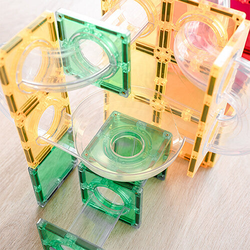 Detail van een Connetix knikkerbaan met gele en groene magnetische tegels en transparante buizen.