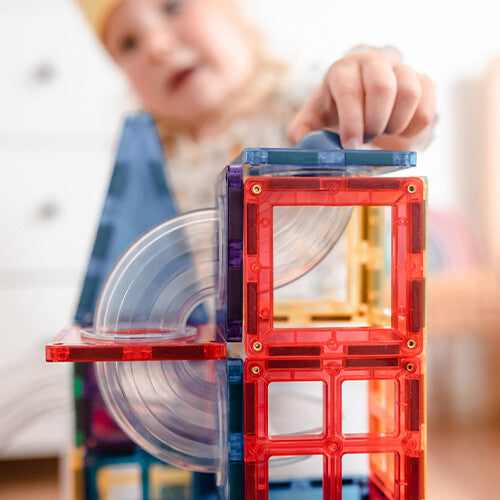 Een kinderhand plaatst een magnetische tegel op een Connetix knikkerbaan, met transparante bochten zichtbaar.