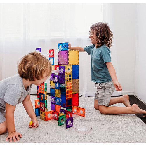 Twee kinderen spelen samen met een grote Connetix knikkerbaan, gebouwd met kleurrijke magnetische tegels en transparante banen.