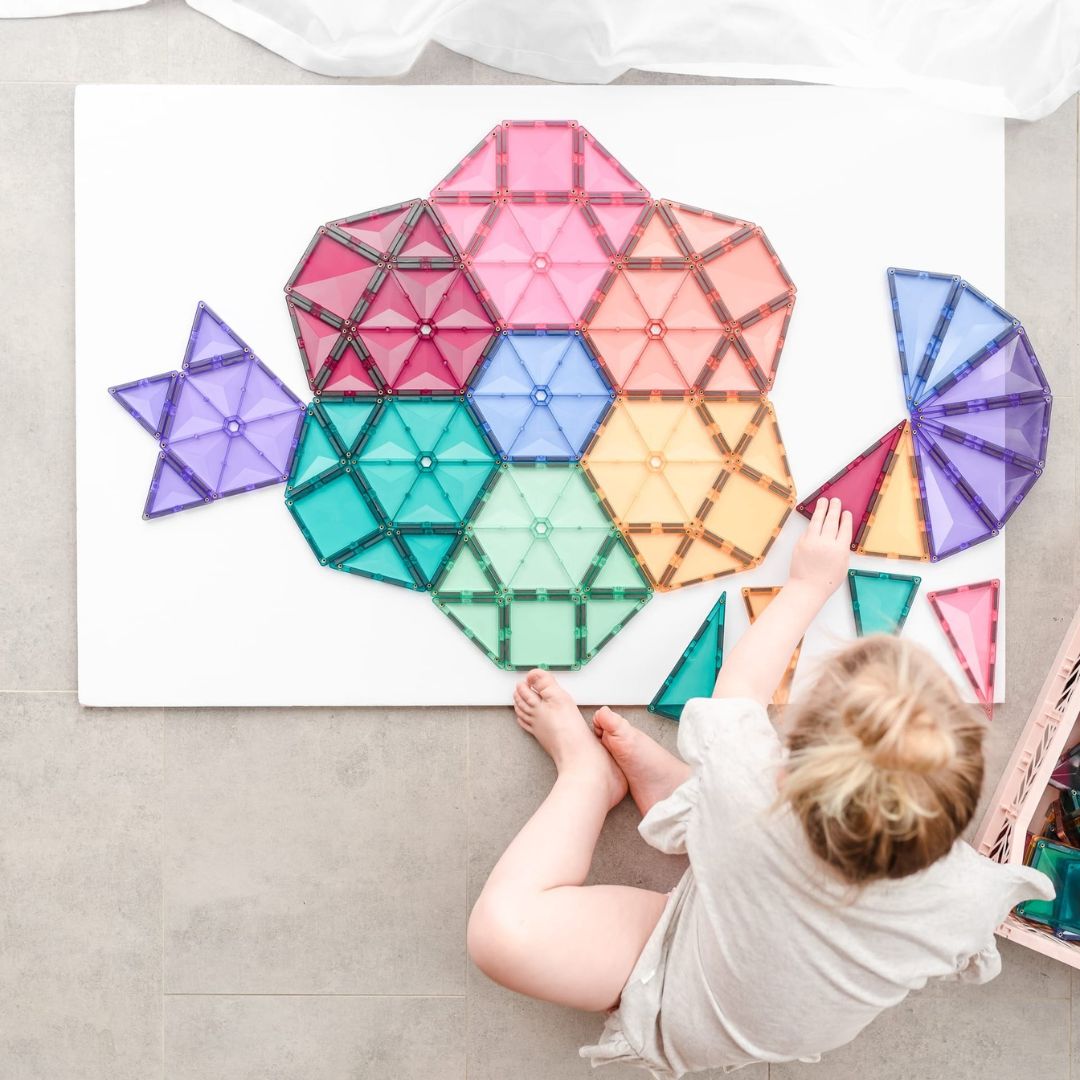 Een kind bouwt een visvormig figuur met Connetix pastel magnetische tegels op een witte ondergrond.