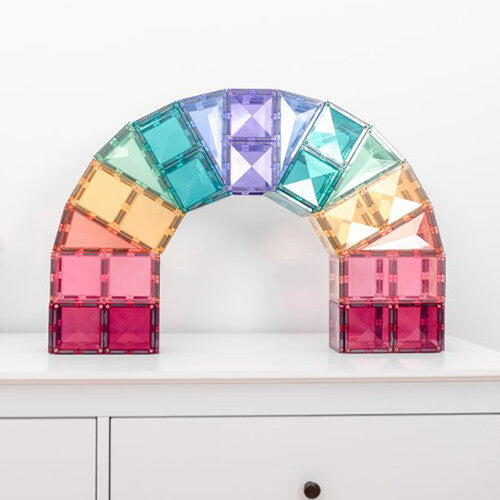 Een regenboogboog gebouwd van Connetix pastel magnetische tegels op een witte ladekast.